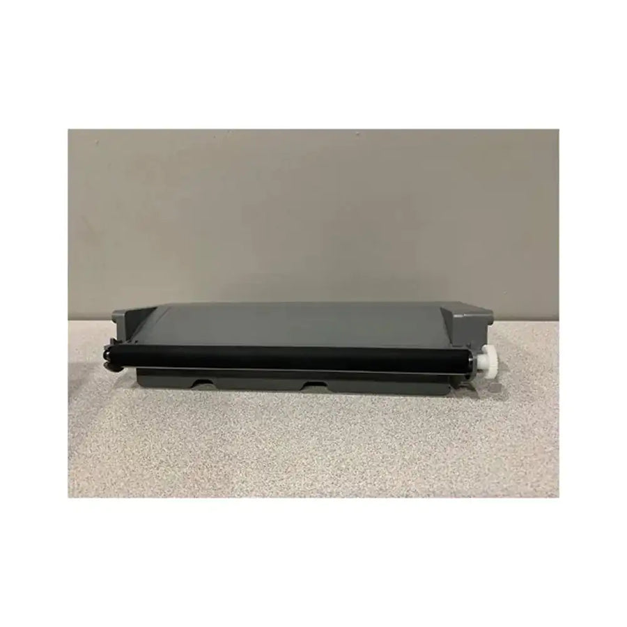 A black toner drum roller with a gray plastic cover and a small white plastic knob, resting on a speckled light gray surface against a solid gray background.