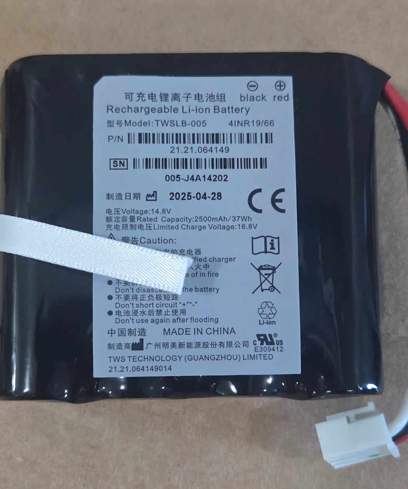 A black rechargeable lithium-ion battery with a white product label, wrapped in a clear protective sleeve with a white tape strip. The label contains Chinese and English text, barcodes, and safety symbols, including 'black red' for the terminal colors and 'TWS TECHNOLOGY (GUANGZHOU) LIMITED' at the bottom.