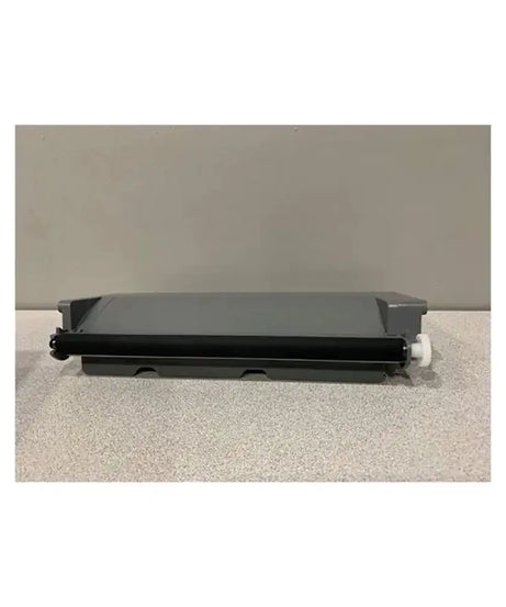 A black toner drum roller with a gray plastic cover and a small white plastic knob, resting on a speckled light gray surface against a solid gray background.