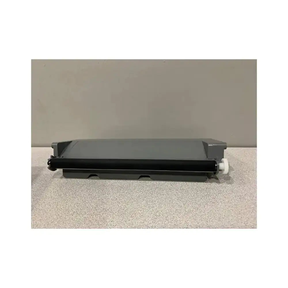 A black toner drum roller with a gray plastic cover and a small white plastic knob, resting on a speckled light gray surface against a solid gray background.