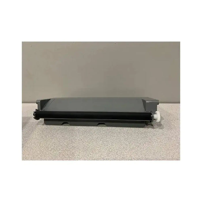 A black toner drum roller with a gray plastic cover and a small white plastic knob, resting on a speckled light gray surface against a solid gray background.